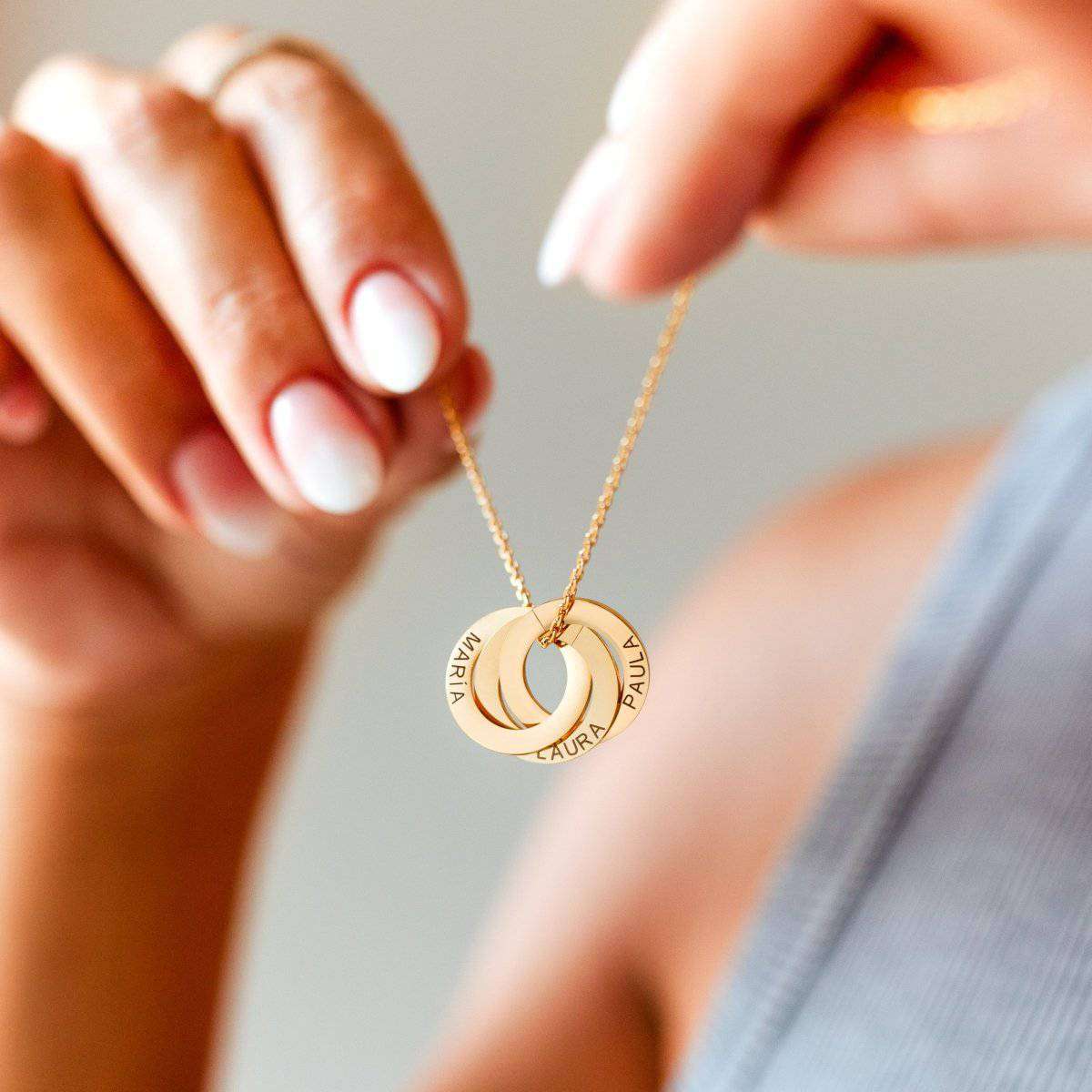 Gold Amity necklace with three linked engraved rings held in hands.